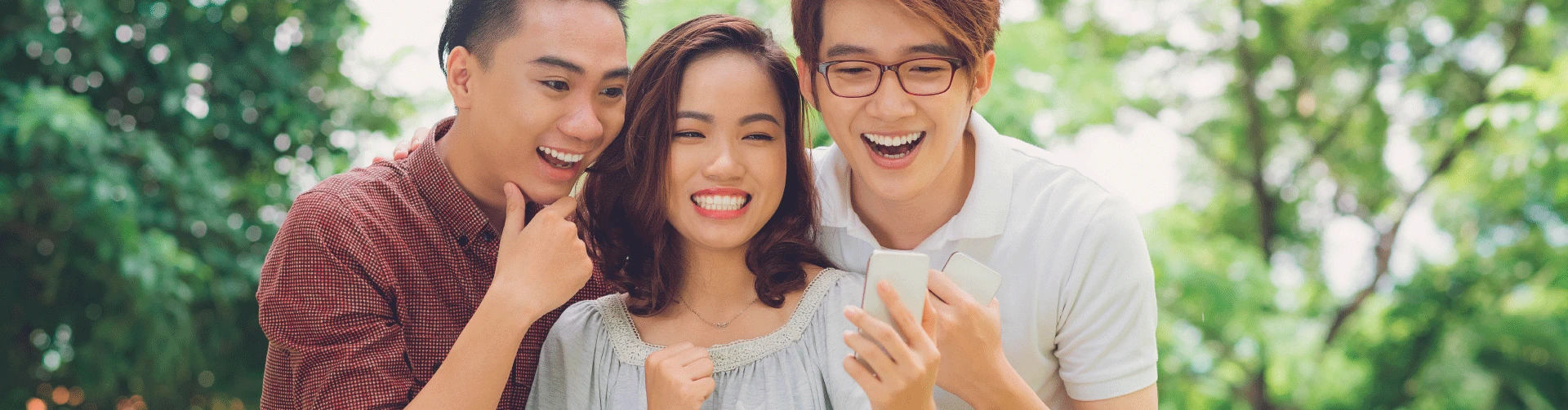 Three people taking a selfie with smiles on their faces while looking at a smartphone.