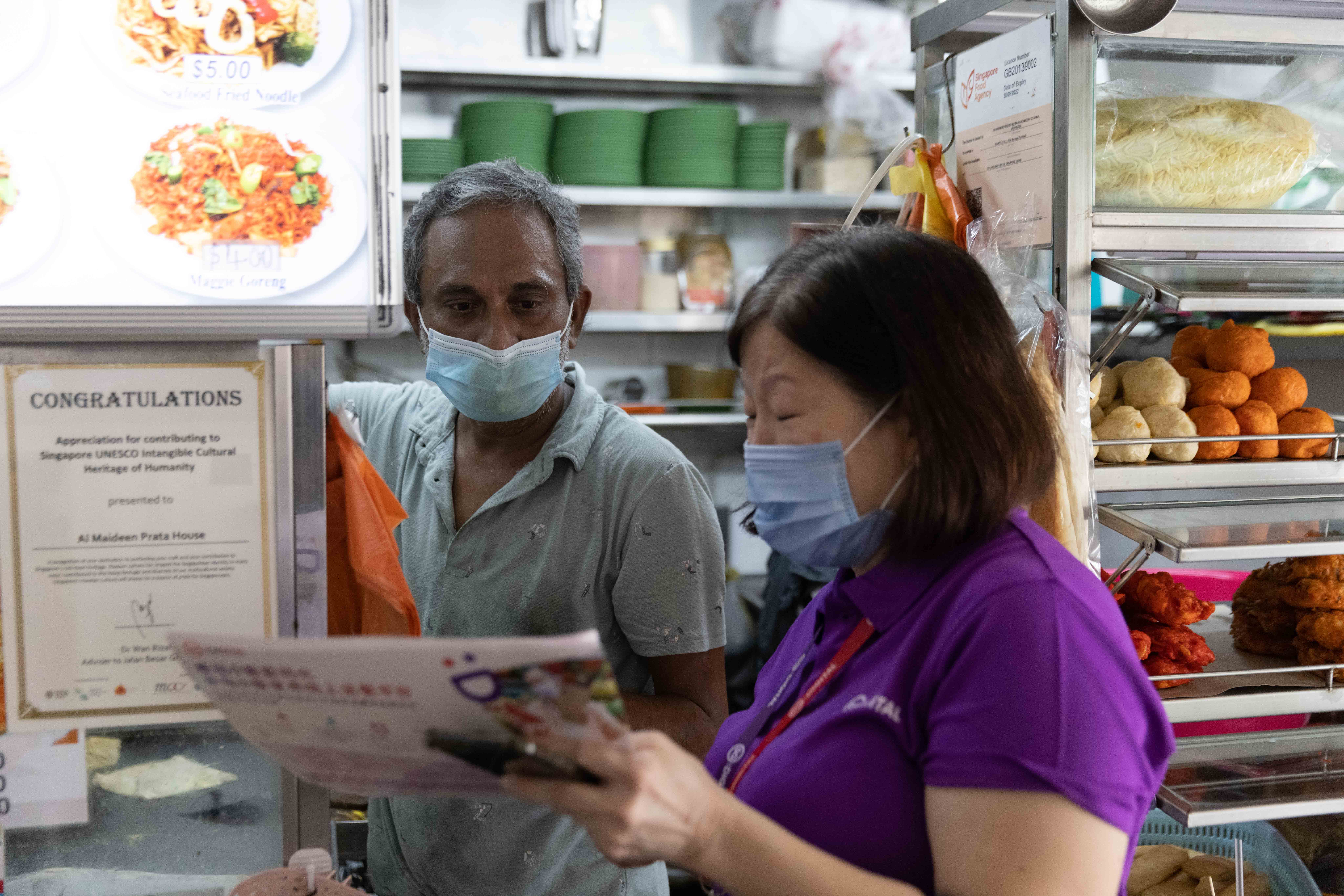A stall owner at a hawker centre is being introduced to the Hawkers Go Digital initiative by an IMDA employee