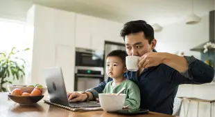 Father using computer with young son on his lap