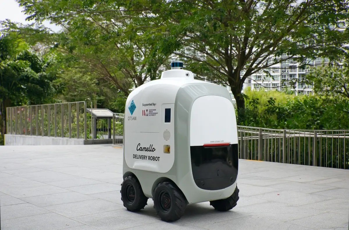 An autonomous mobile delivery robot moving along a footpath with a package on top.