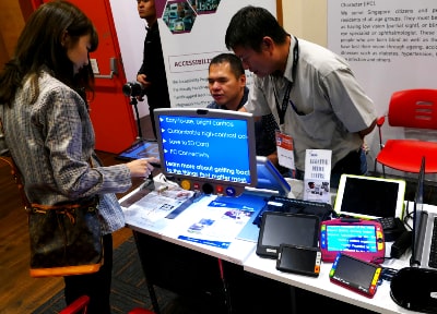 E2Connect Forum 2018: Two individuals introducing a lady to assistive technology at a booth
