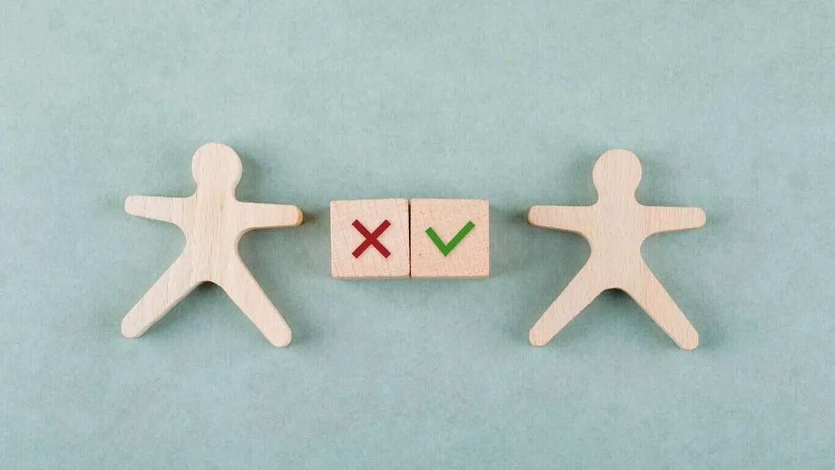 Two wooden human stick figures with two wooden blocks, one marked with an X and the other with a tick