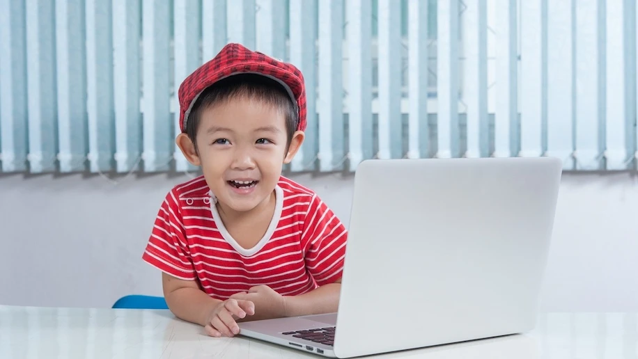 A little boy smiling in front of a laptop, participating in the Code for Fun Enrichment Programme in SG to improve digital literacy skills