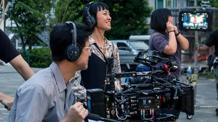 A videographer and a producer are looking at the scene setup of Wonderland, a Made with SG film. The videographer is seated with a video camera, while the producer wearing a headset. 