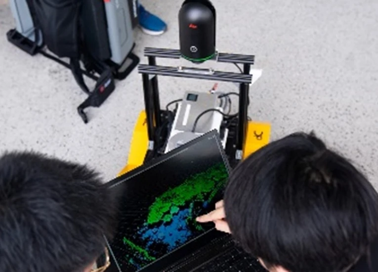 Two students observe a laptop screen to monitor a Simultaneous Localisation and Mapping (SLAM) robot in its settings.