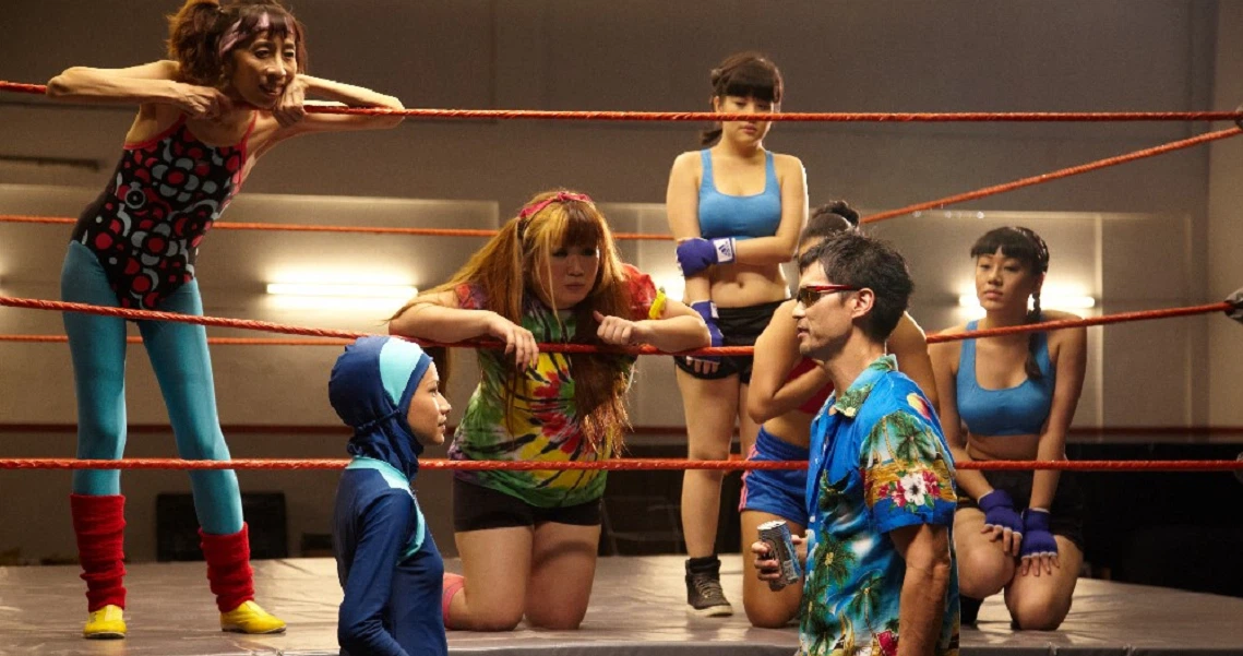 A diverse group of wrestlers in colorful outfits gather in a boxing ring for a scene from the film Banting.