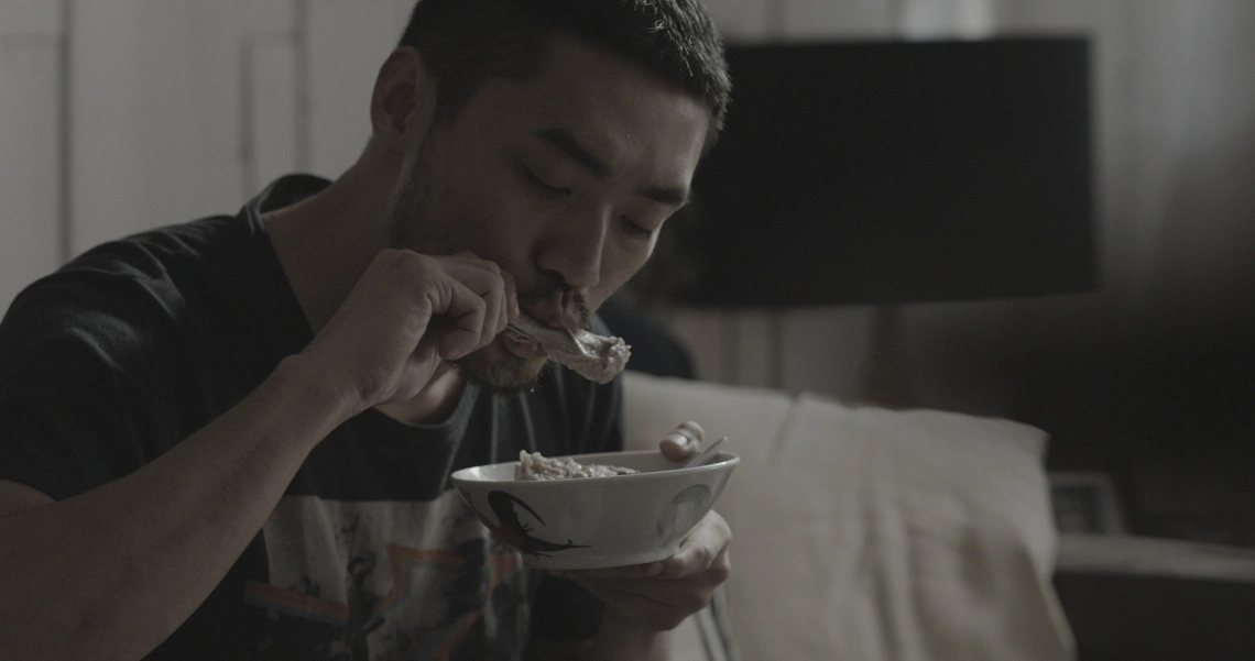 A man eats from a bowl in a dimly lit room, capturing a tense moment from the Singaporean film "Lang Tong".