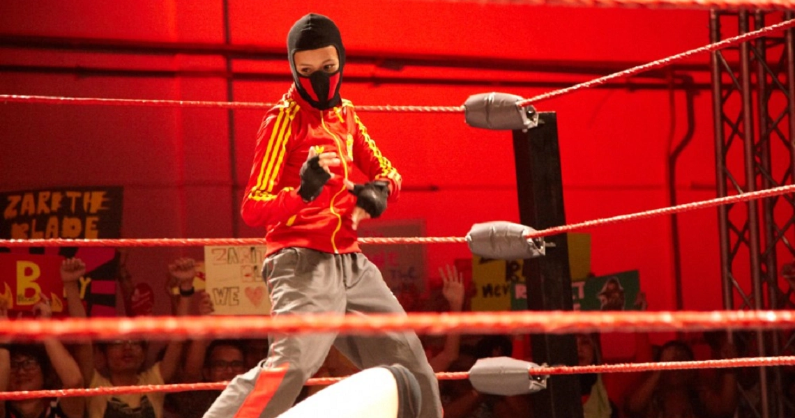 A boxer in a yellow and red outfit stands in a boxing ring from the film Banting, illuminated by dramatic red lighting.