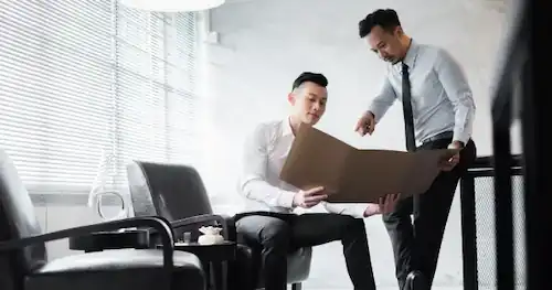 Two professionals in a meeting room examining a folder, engaging in a discussion about IMDA regulations