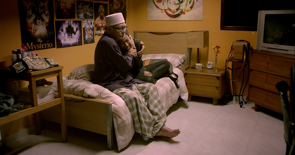 A poignant scene from the film Banting shows two characters embracing on a bed in a teenager's room decorated with wrestling posters.