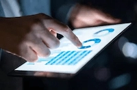 A pair of hands holding an iPad, displaying IMDA's key business graphs and statistics