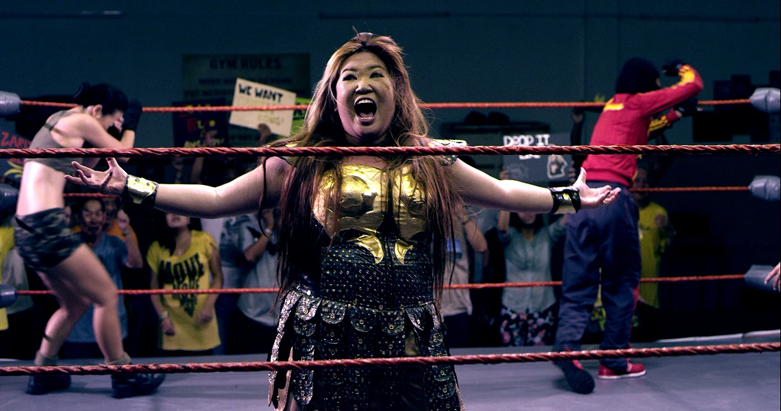Intense scene from the film Banting showing a female wrestler in a gold costume shouting triumphantly in a wrestling ring.