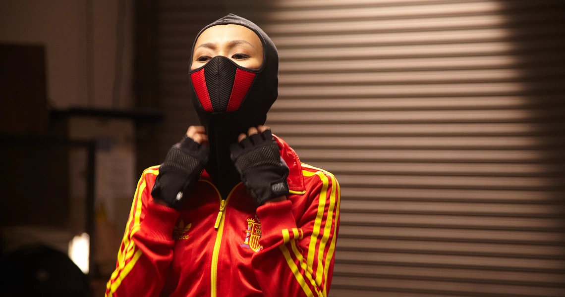 A still from the film Banting shows a person in a red and yellow sports jacket wearing a black and red face mask.